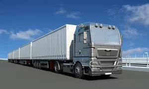 A long semi-truck with a silver cab and white trailers is parked on a paved road under a clear blue sky.