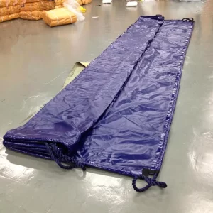 A large folded blue tarpaulin lies on the floor with ropes attached at the edges. Rolled and packaged items can be seen in the background.