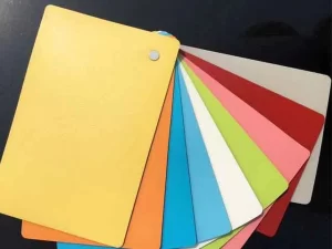 A fanned-out set of color sample cards, including yellow, orange, light blue, dark blue, white, red, pink, green, and beige, on a dark surface.