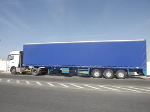 A large blue semi-trailer truck is parked on a road under a clear sky.