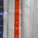 Close-up of the Clear String Reinforced Poly Tarp – 7 oz FR Scaffold Sheeting, featuring blue and red reinforced edges with evenly spaced holes. The main material is a semi-transparent, woven plastic.