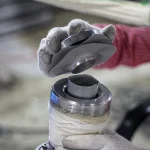 A person wearing gloves holds a metal component above a Custom Truck Tarp and Trailer Tarp in a workshop setting.