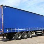 A large truck equipped with a Custom Truck Tarp and Trailer Tarp, parked on a concrete surface under a clear sky.