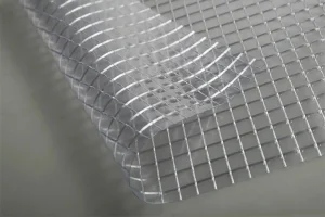 Close-up of FR SCAFFOLD SHEETING-10oz, partially lifted at the corner, revealing its transparent grid pattern on a flat surface.